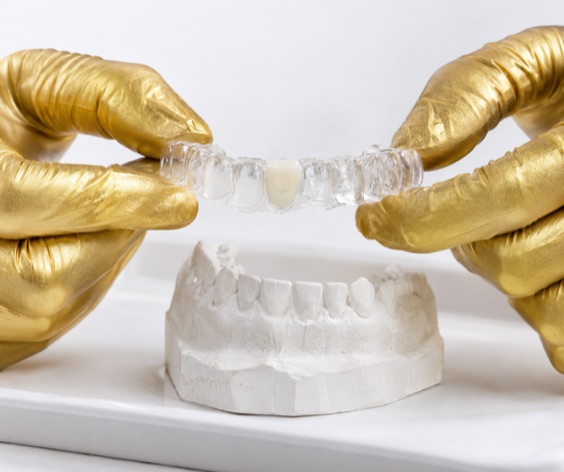 Clear Essix retainer with one built-in tooth lifted off a stone model