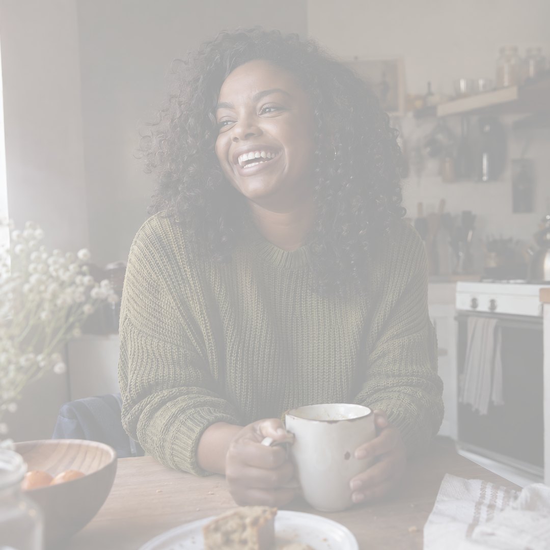 A woman laughing over a mug at a kitchen table